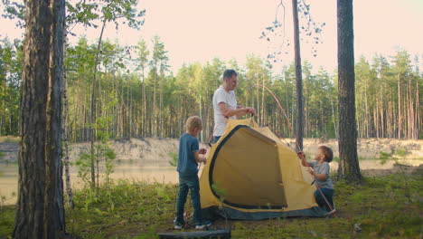 The-children-together-with-their-father-set-up-a-tent-for-the-night-and-camping-in-the-forest-during-the-journey.-A-man-and-two-children-3-5-years-old-together-in-a-hike-gather-a-tent-in-slow-motion